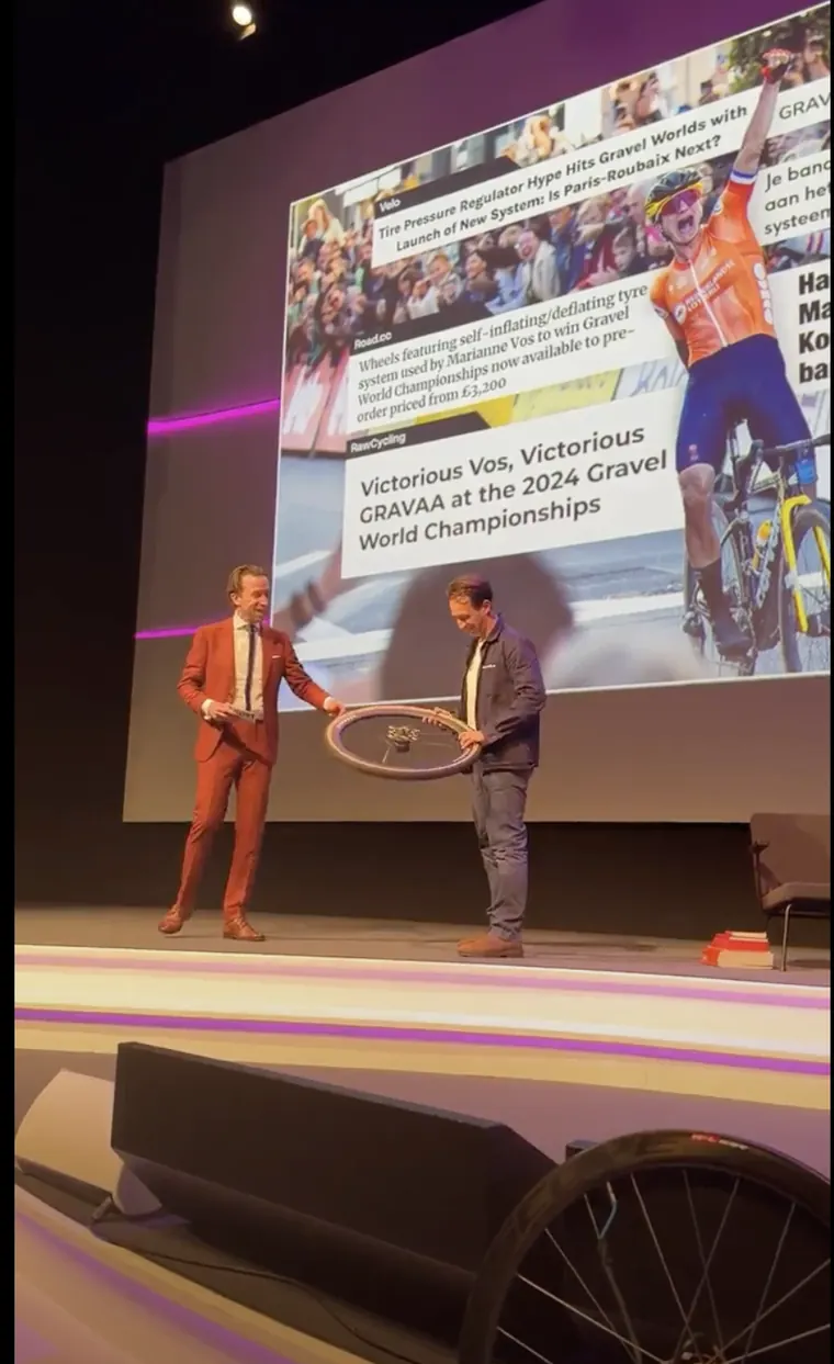 Loek Luijbregts on stage holding a GRAVAA wheel in front of a screen full of press coverage
